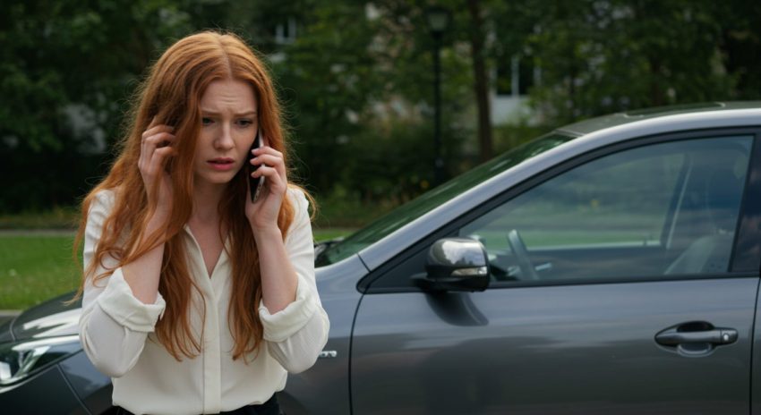 ハイブリッド車のエンジンがかからないので悩んだ顔で電話をする女性の画像